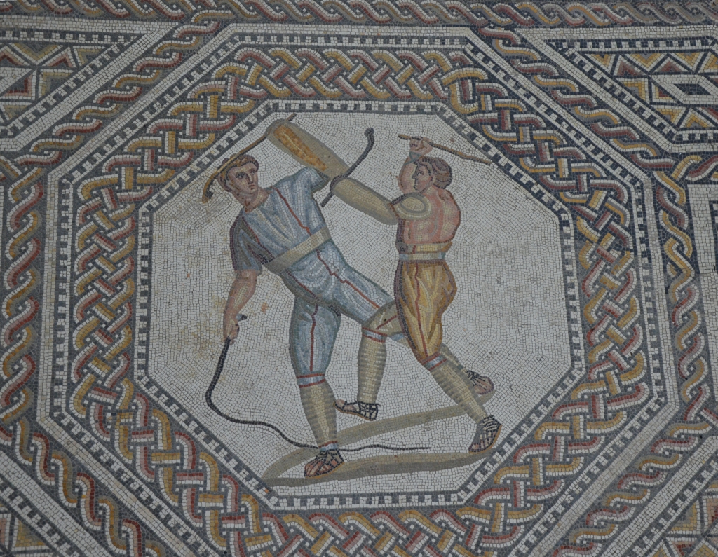 Two_combatants_attacking_one_another_with_cudgels_and_a_whip,_the_gladiator_mosaic_at_the_Roman_villa_in_Nennig,_Germany_(9288895115)